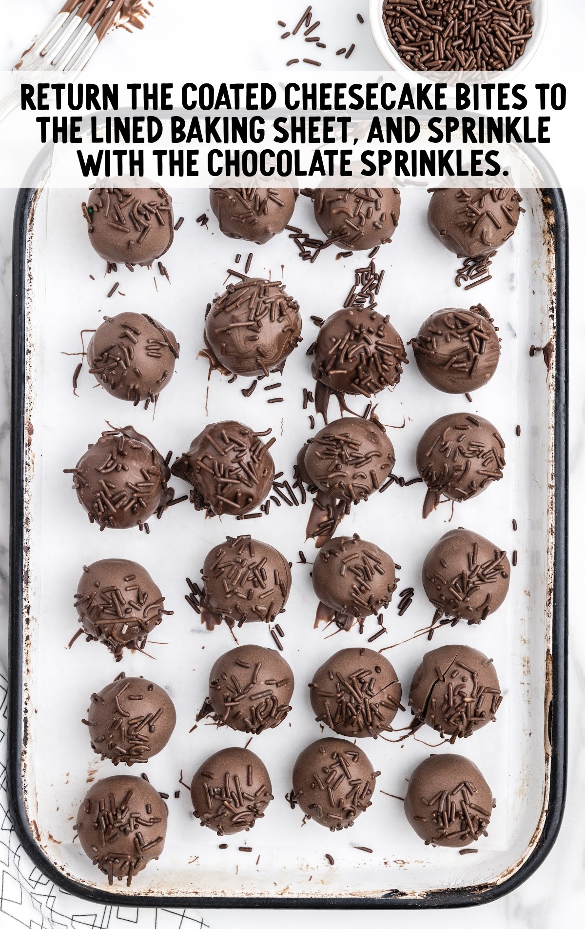 coated cheesecake bites topped with chocolate sprinkles on a parchment lined baking sheet
