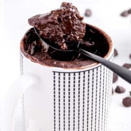 close up shot of a chocolate cake in a mug with a piece being taken out with a spoon