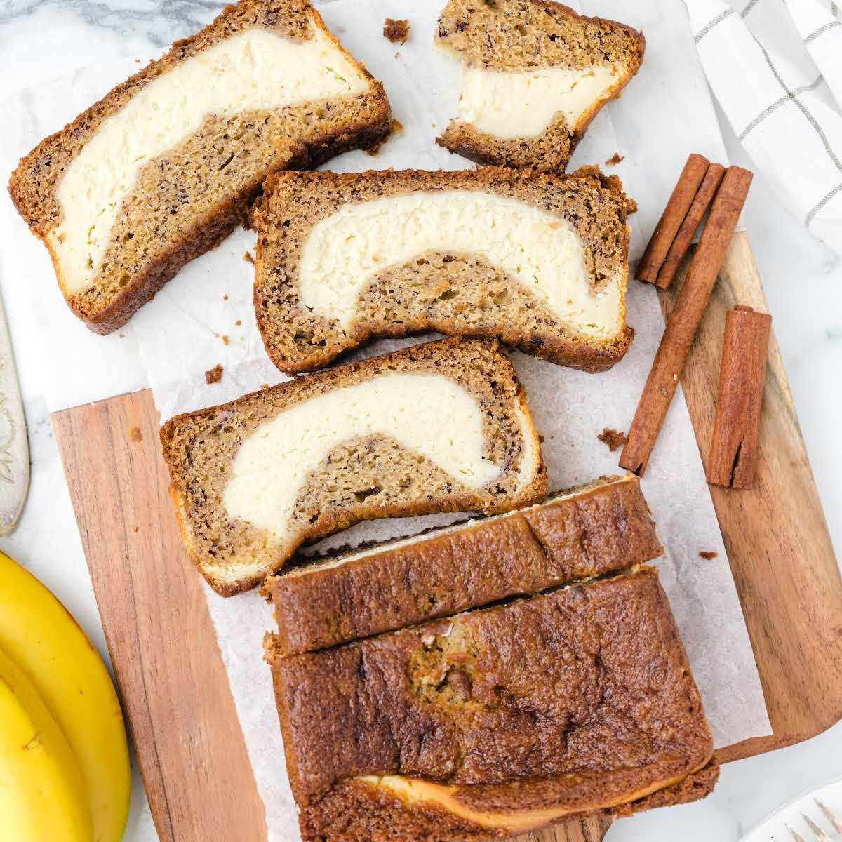 close up overhead shot of slices of bread taken out of a loaf on a wooden board with cinnamon sticks