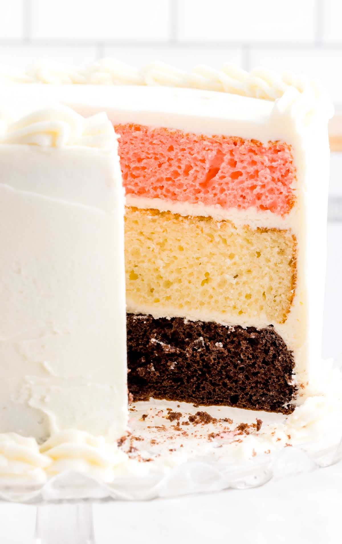 close up shot of a Neapolitan Cake with a slice missing on a cake stand