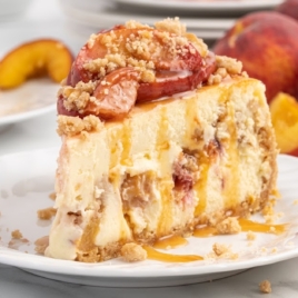 A slice of Peach Cobbler Cheesecake on a dessert plate garnished with caramel sauce.