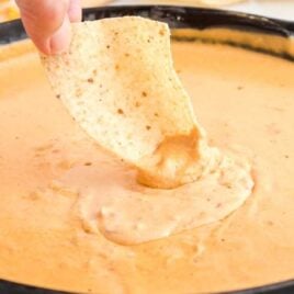 close up shot of a chip dipped into a skillet of queso dip