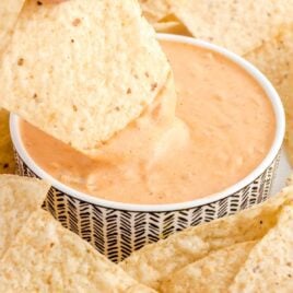 close up shot of a chip dipped into a bowl of queso dip