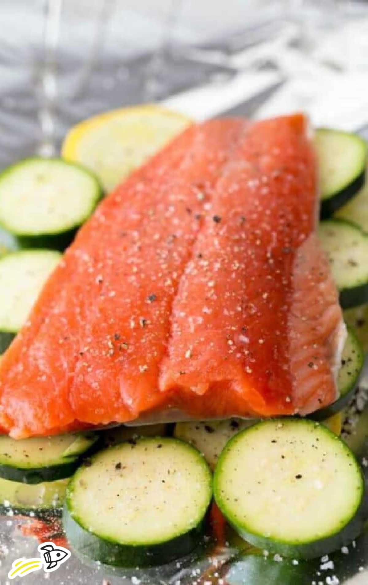close up shot of a uncooked salmon placed on top of sliced zucchini