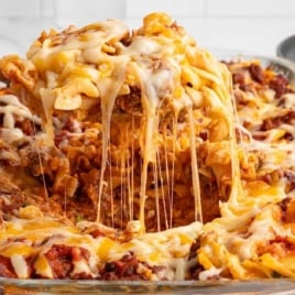 Bubbly sour cream noodle bake in a glass casserole dish with melted cheese being scooped up.
