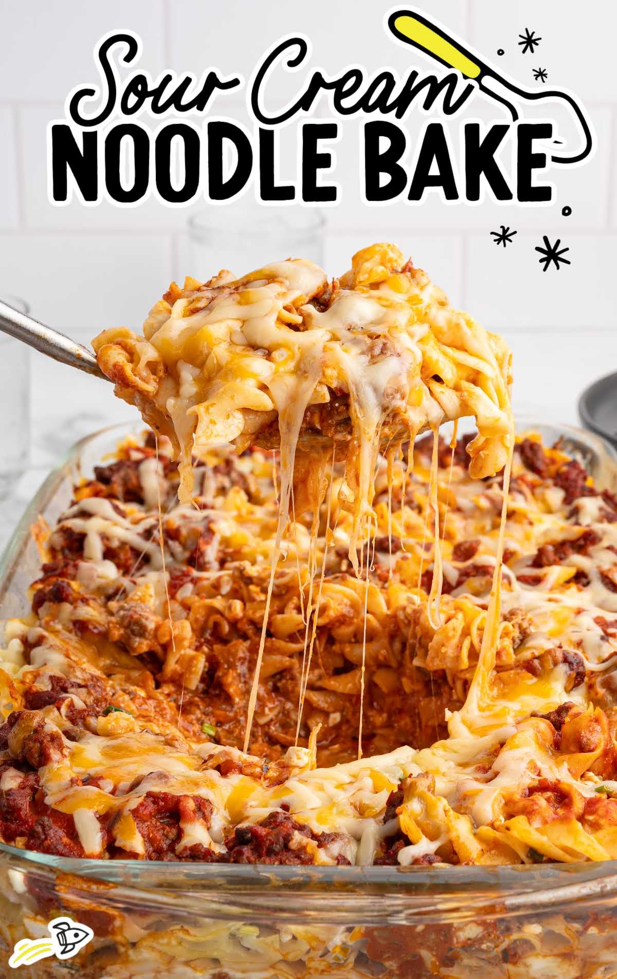 Cheesy sour cream noodle bake with stretchy melted cheese lifting from the pan.
