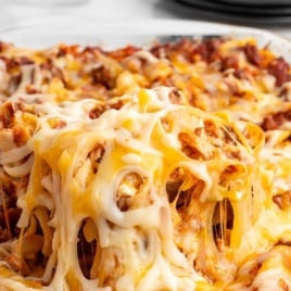 Cheesy sour cream noodle bake in a glass casserole dish with melted cheese stretching over the top, labeled as an easy dinner casserole.