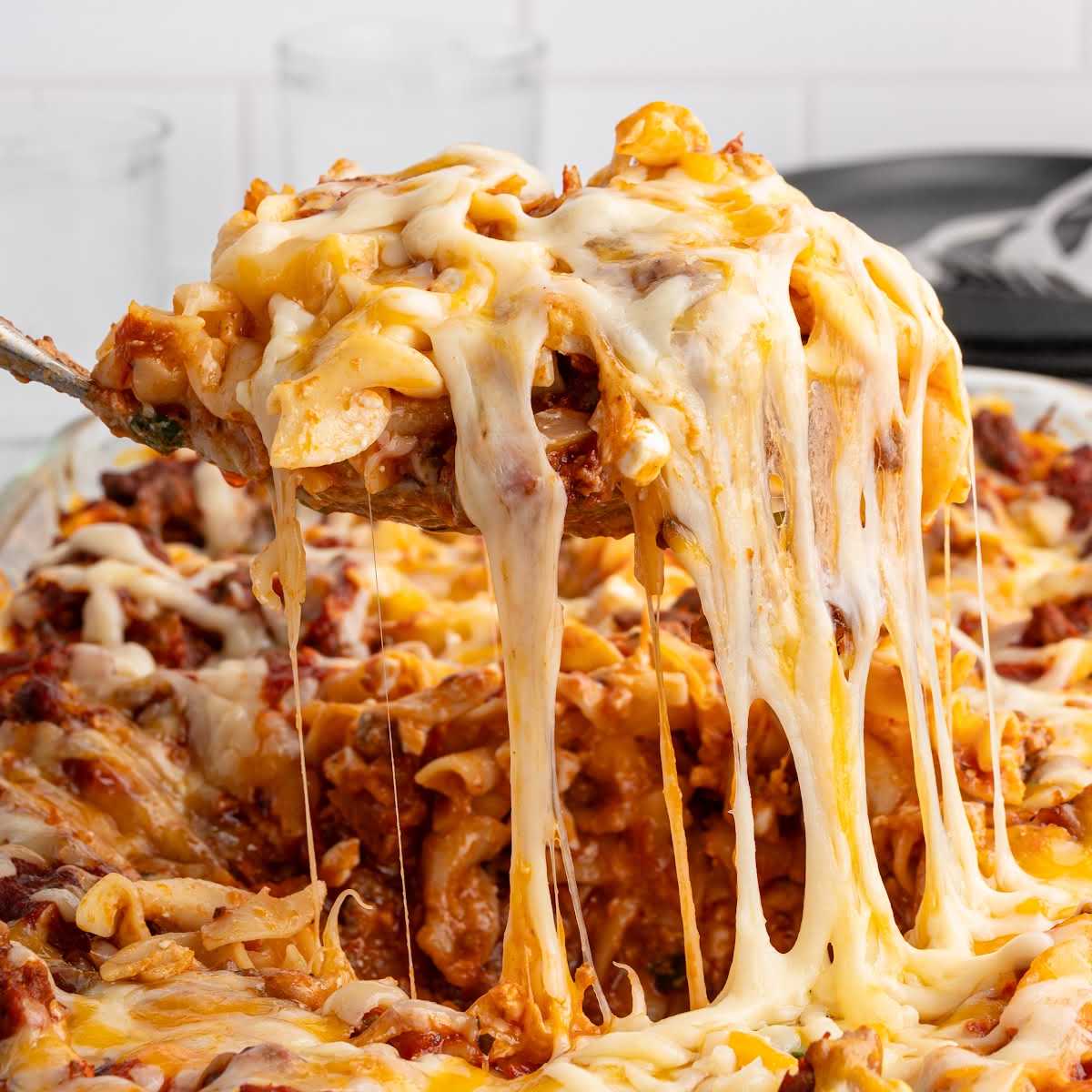 Cheesy serving of sour cream noodle bake being lifted from the pan showing stretchy melted cheese.