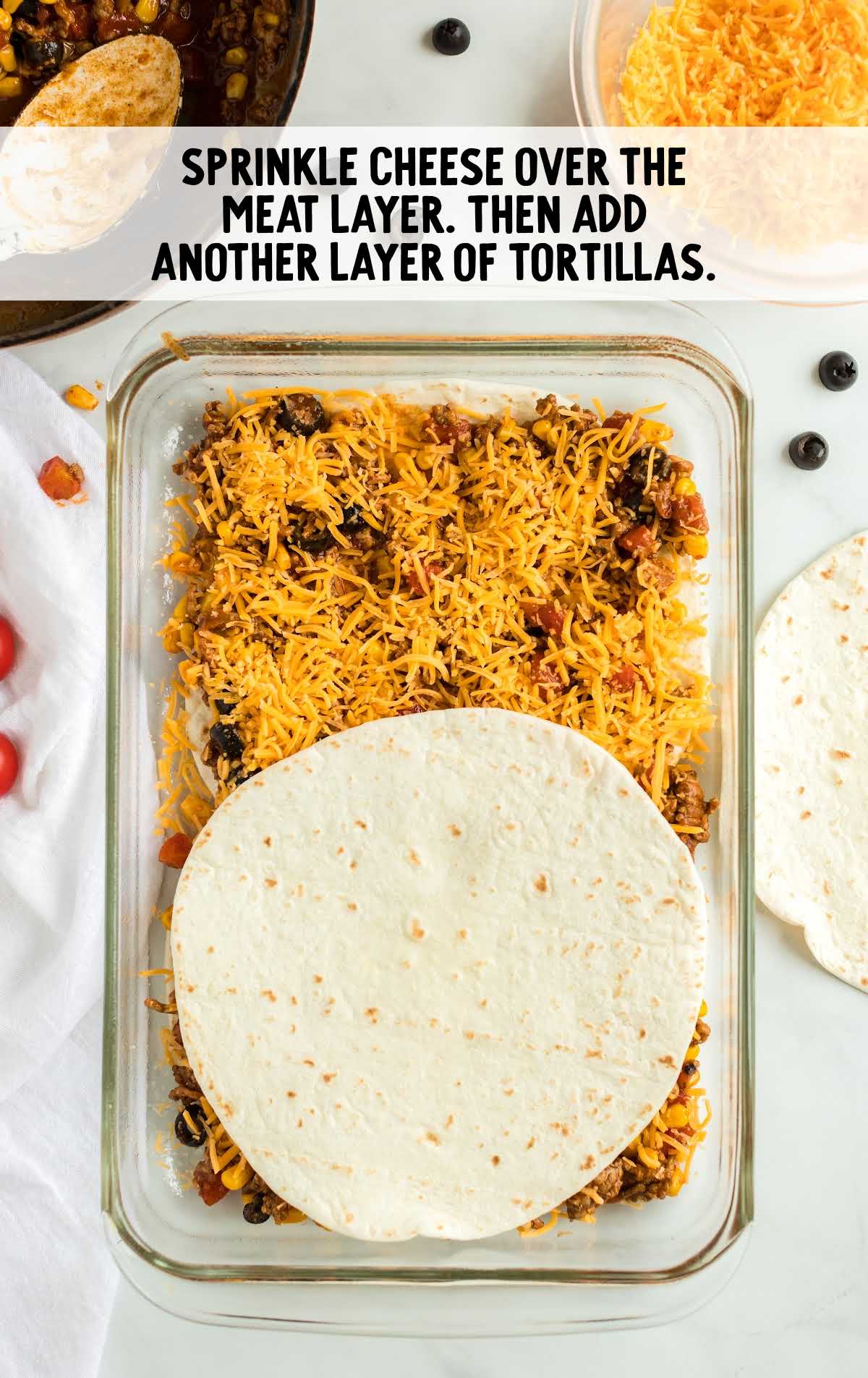 cheese and tortillas placed on top of the meat mixture in a baking dish