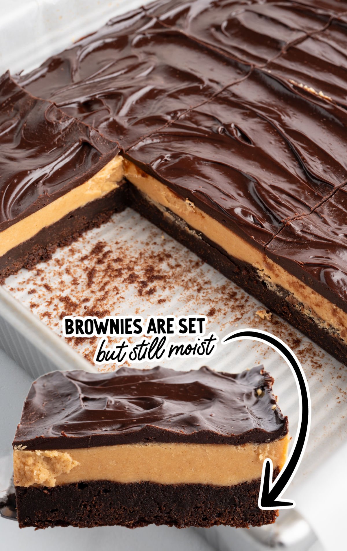 Buckeye brownies in a baking pan with smooth chocolate ganache, creamy peanut butter layer, and fudgy brownie base, with one slice pulled out to show layers