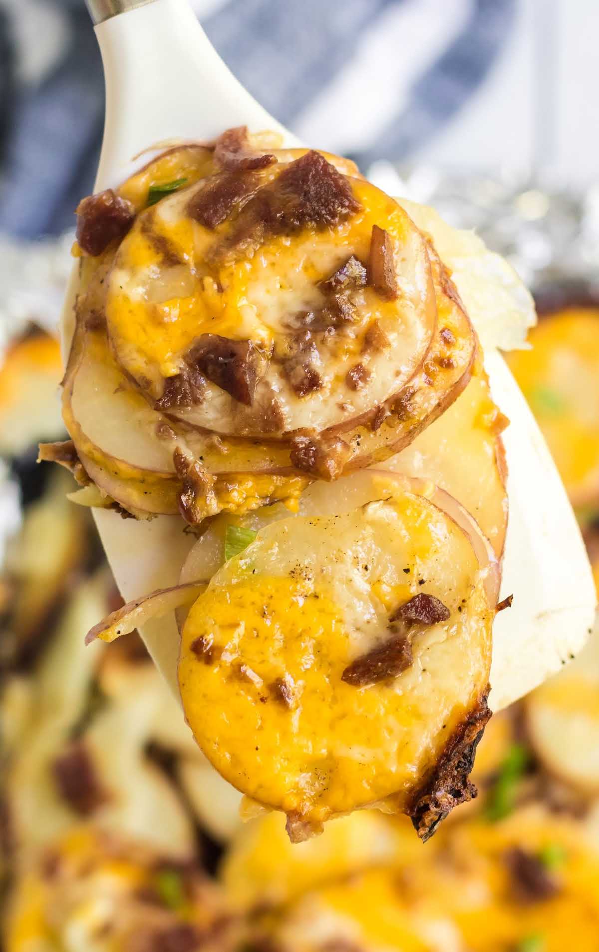 overhead shot of potatoes topped with cheese, bacon bites, and green onions on a spatula