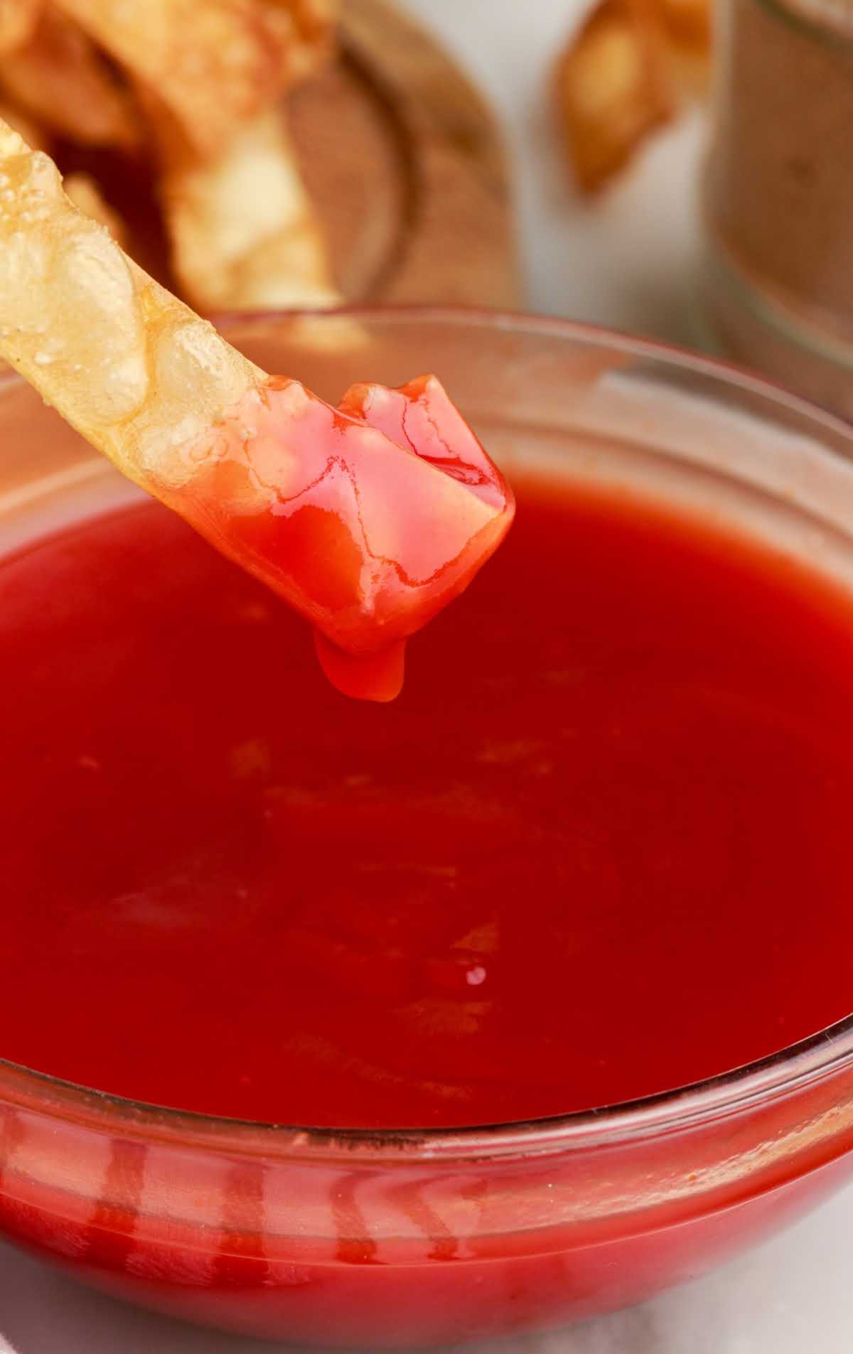 close up shot of a bowl of homemade sweet and sour sauce with a chip dipped into the sauce