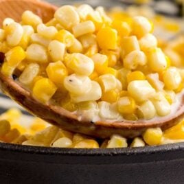 close up shot of corn in a skillet and a spoonful on a large wooden spoon