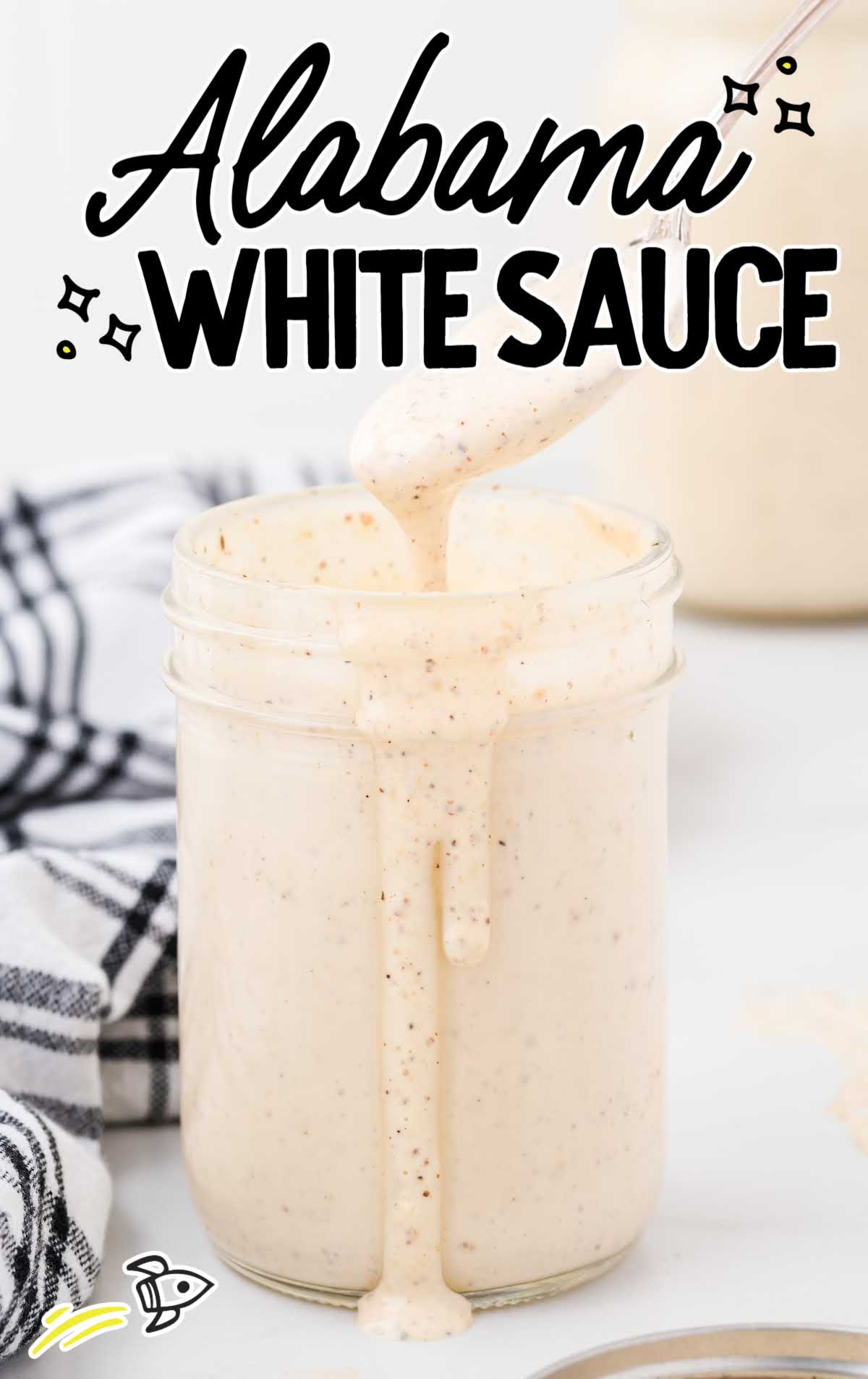 a spoon full of Alabama White Sauce with Alabama White Sauce in a jar