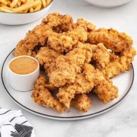 A bunch of Chicken Tenders on a plate with sauce