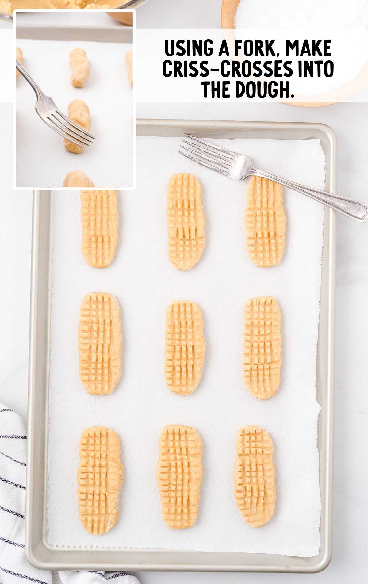 cookies in a baking pan with a fork making lines on dough