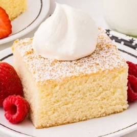 Plate of hot milk cake with a dollop of whipped cream and fresh strawberries and raspberries on the side.