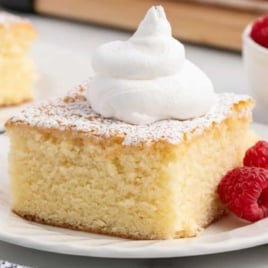 Moist hot milk cake square topped with whipped cream and served with fresh raspberries.