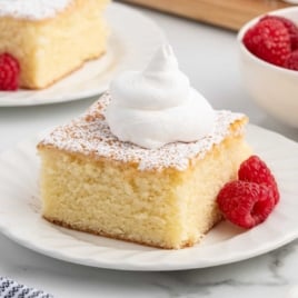 Hot milk cake slice with powdered sugar and whipped cream for the recipe card header image.