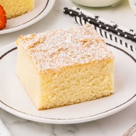 Top-down shot of a hot milk cake slice on a white plate, styled with a star-patterned napkin and a fork on the side.