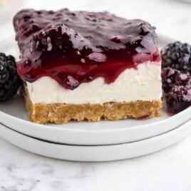 close up shot of a slice of blackberry cheesecake on a plate with a blackberry