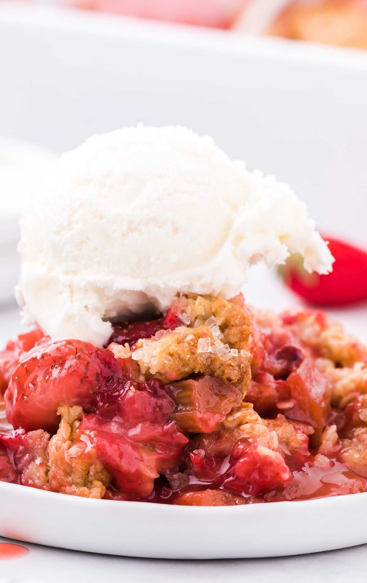 close up shot of a serving of Rhubarb Strawberry Crisp topped with vanilla ice cream on a plate
