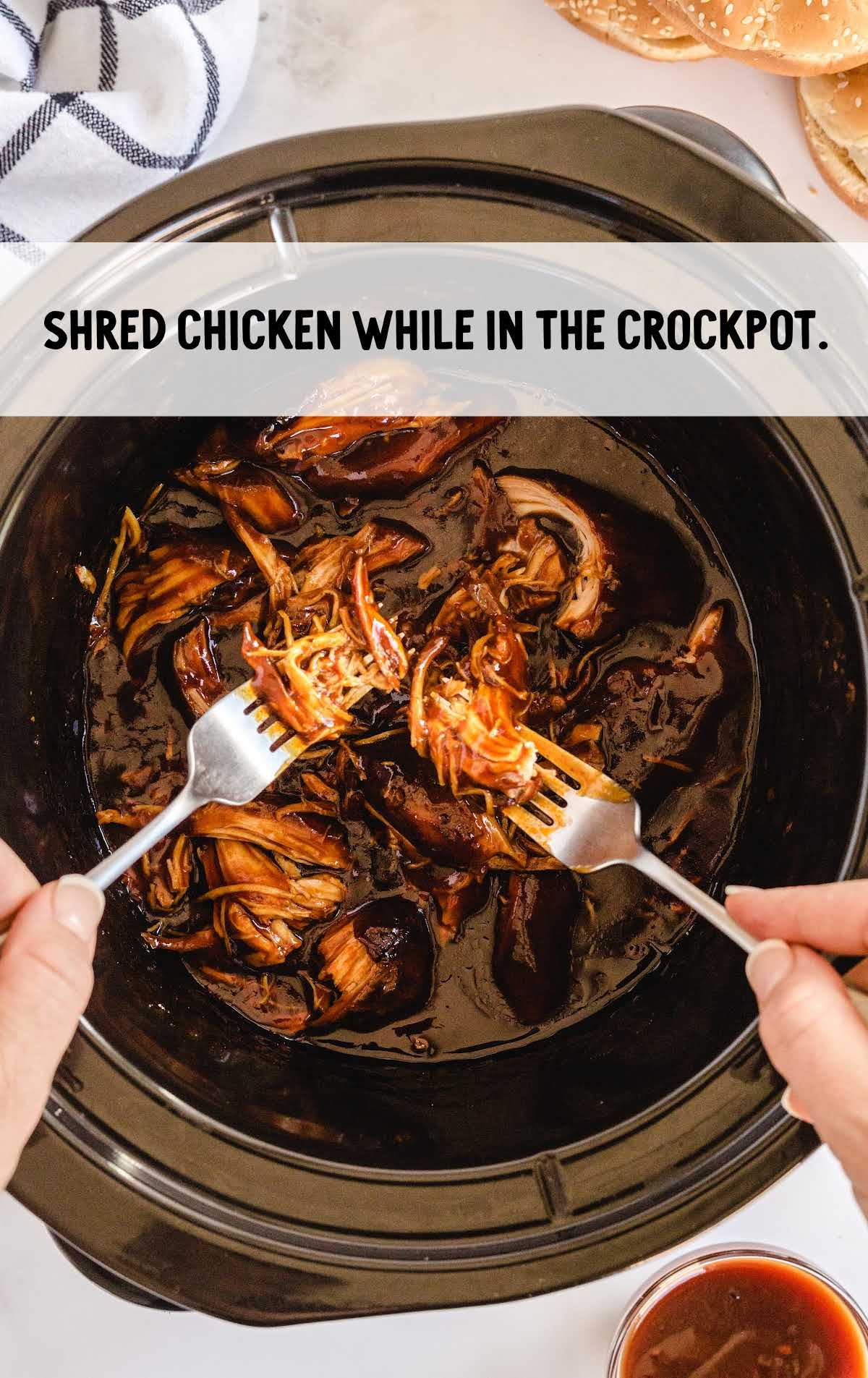cooked chicken being shredded in the slow cooker