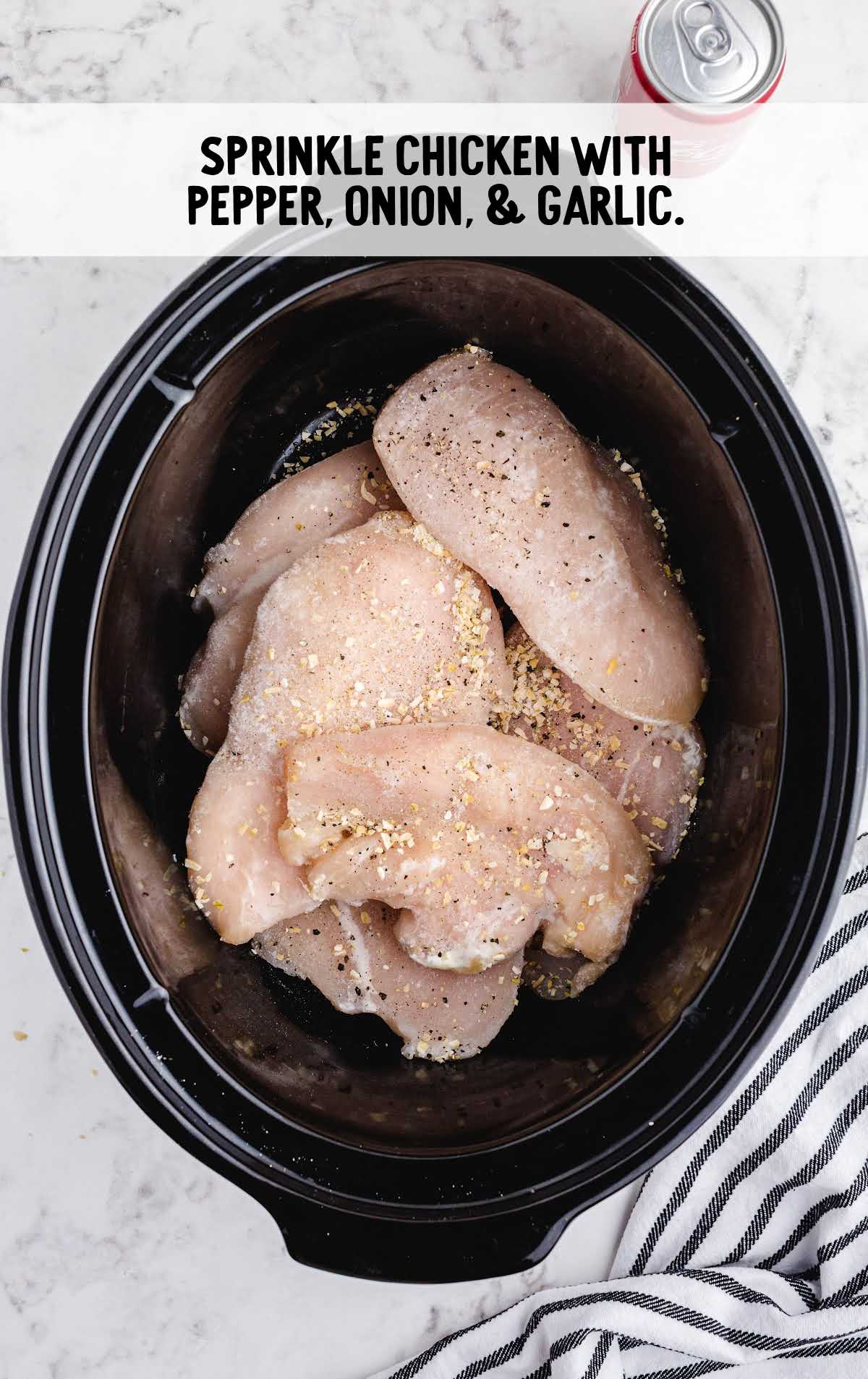 chicken breast sprinkled with pepper, onion, and garlic in a slow cooker