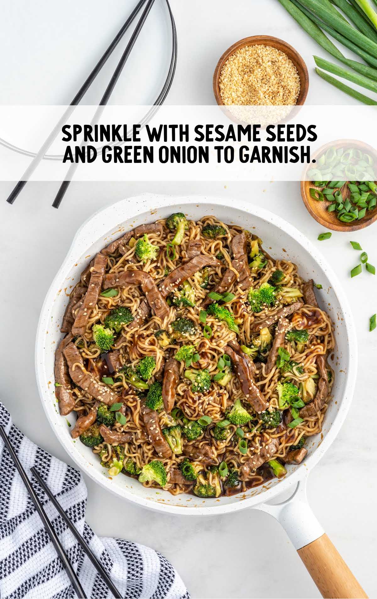 beef ramen stir fry garnished with sesame seeds and green onions in a skillet