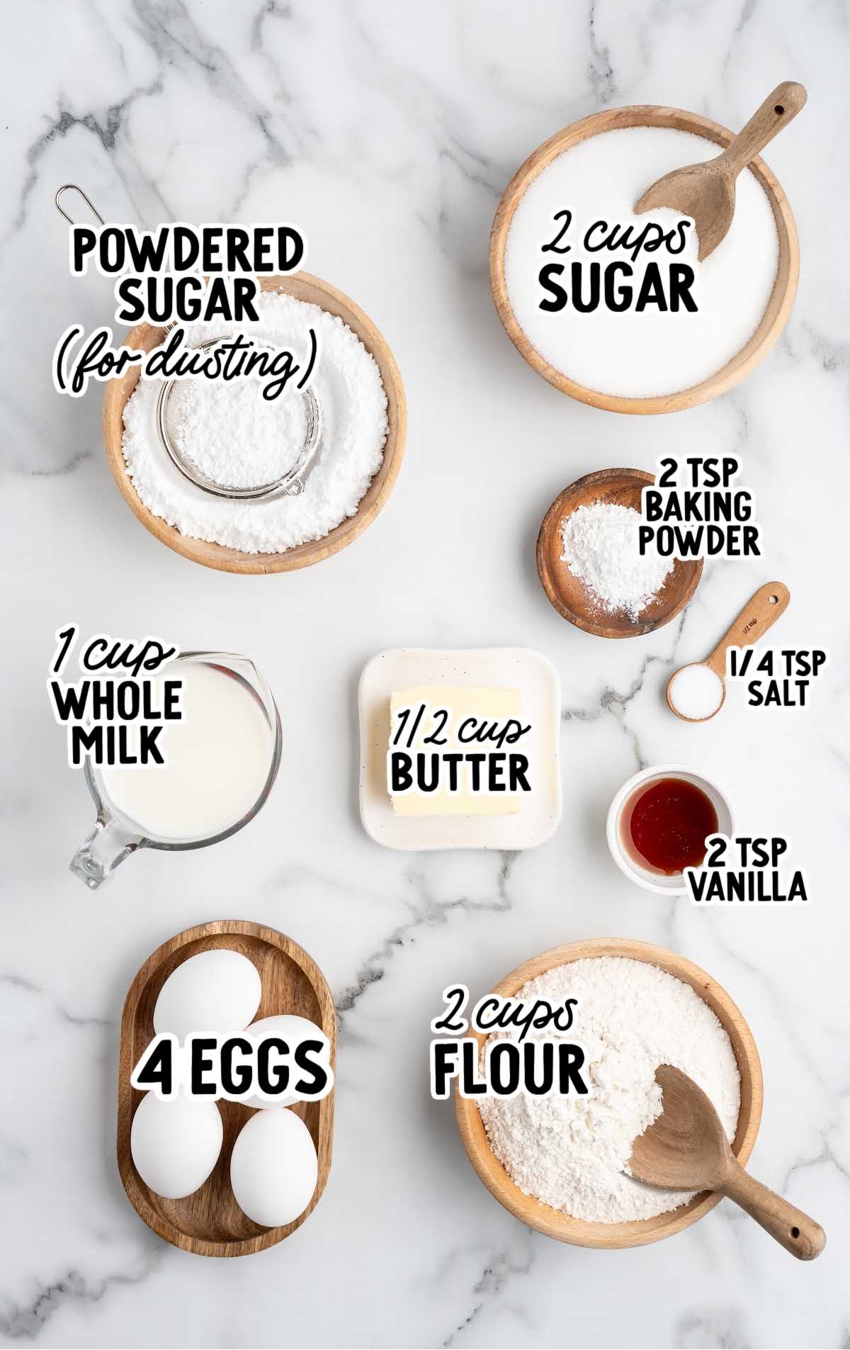 Overhead view of hot milk cake ingredients measured out and labeled on a marble surface.