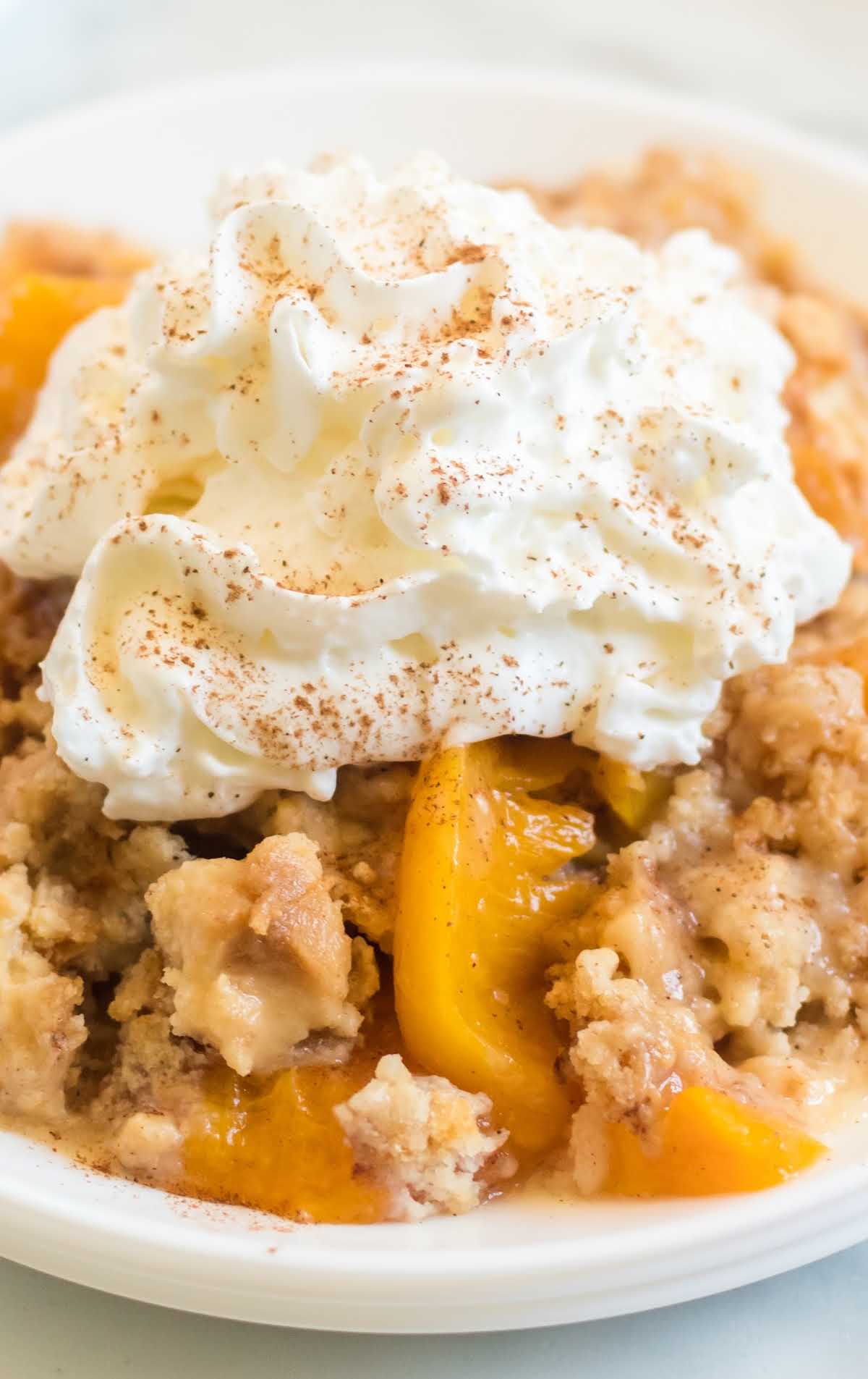 close up shot of a serving of peach dump cake topped with whipped cream