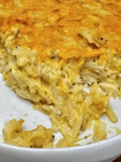 A close-up of a cheesy Cracker Barrel Hashbrown Casserole in a white dish, with a serving scooped out, showing its creamy and golden-brown baked top.
