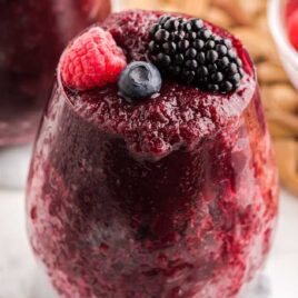a close up shot of red wine slushie topped with mixed berries in a glass cup