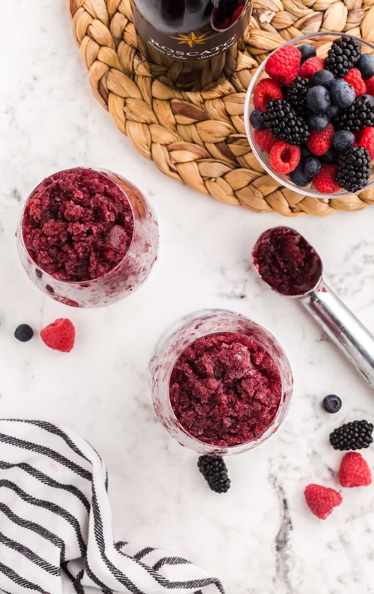 overhead shot of red wine slushies in a glass cup with mixed berries on the side