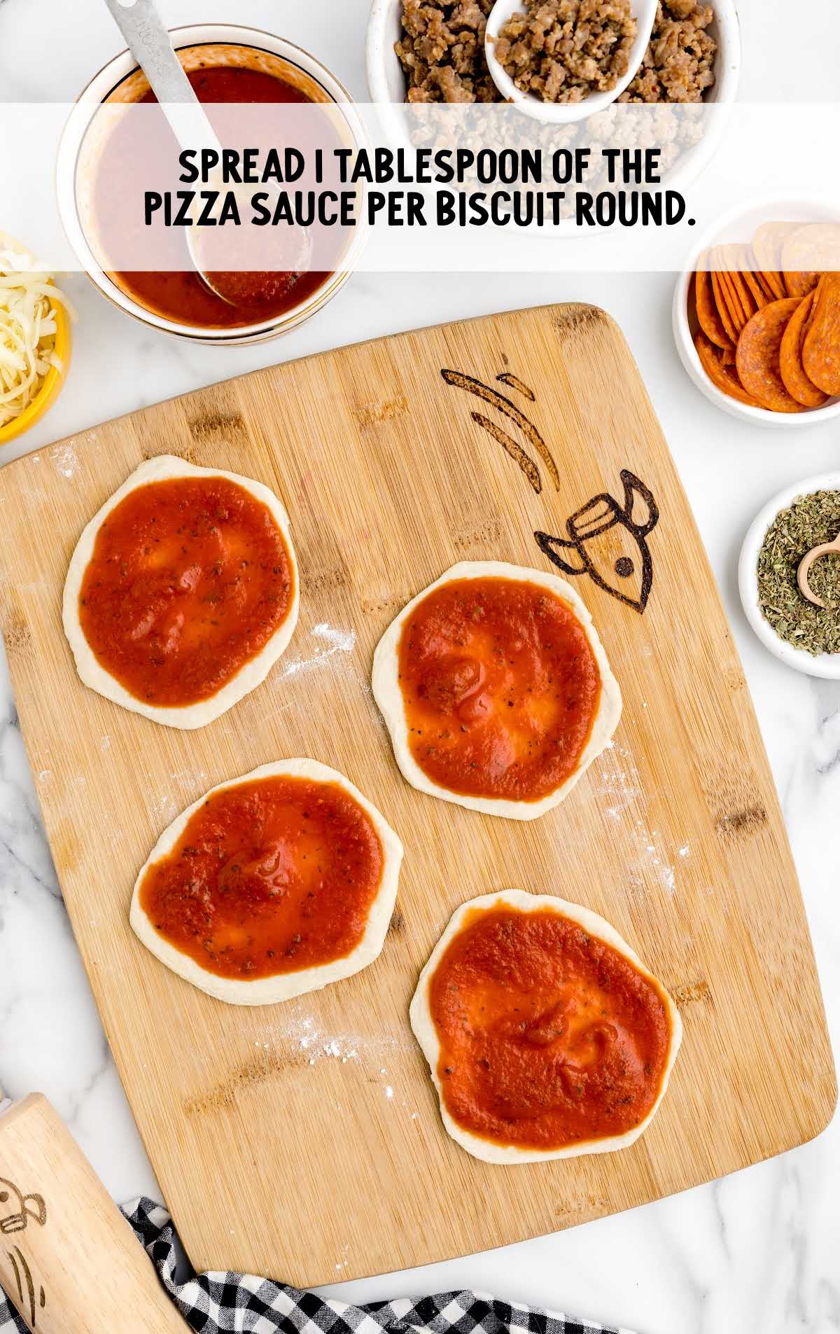 pizza sauce spread on the biscuit round on a wooden board
