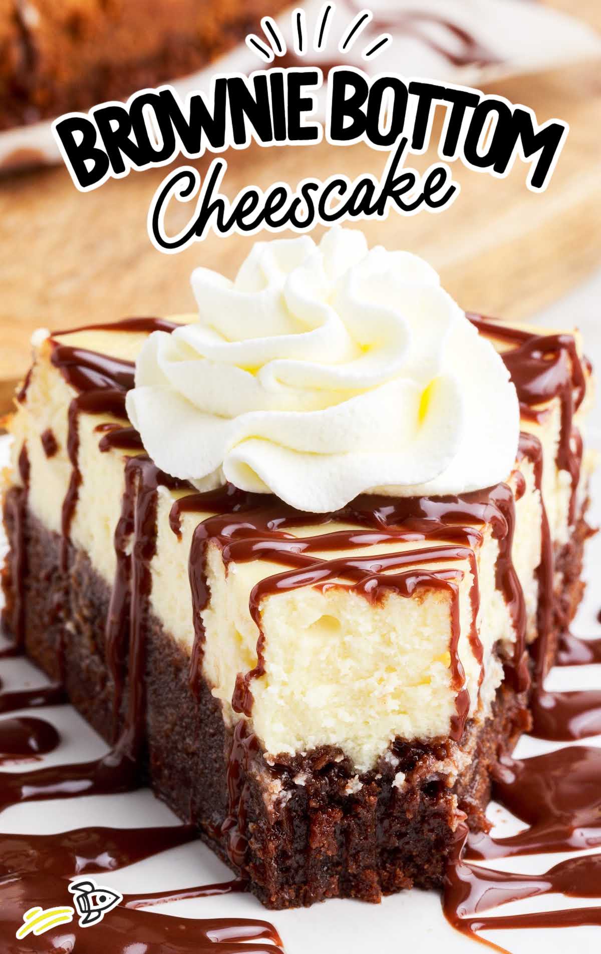 a slice of Brownie Bottom Cheesecake drizzled with chocolate fudge topped with whipped cream