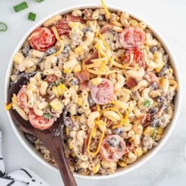 overhead shot of Cowboy Pasta Salad in a bowl with a large wooden spoon