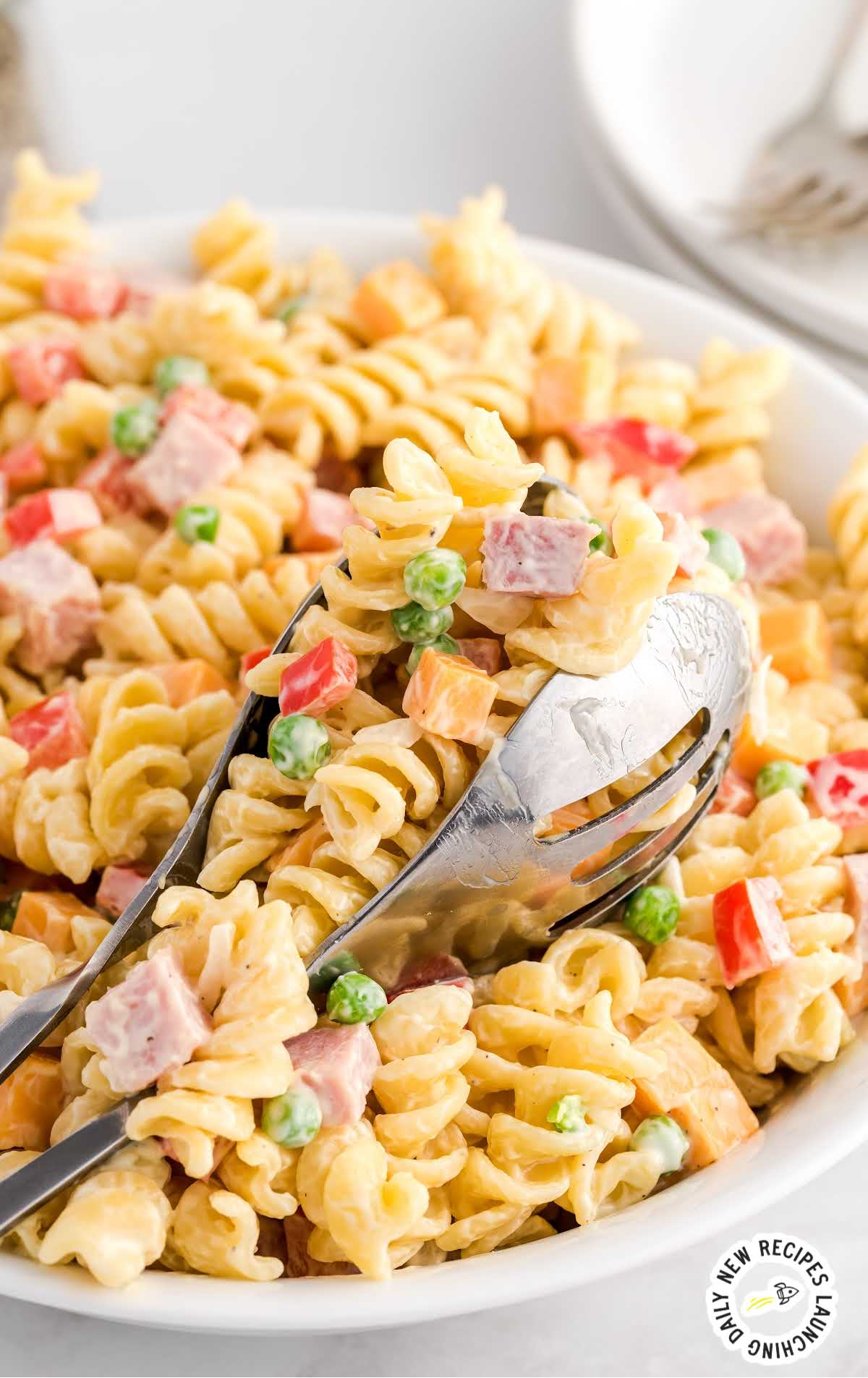 close up shot of tongs grabbing a piece of Loaded Pasta Salad in a bowl