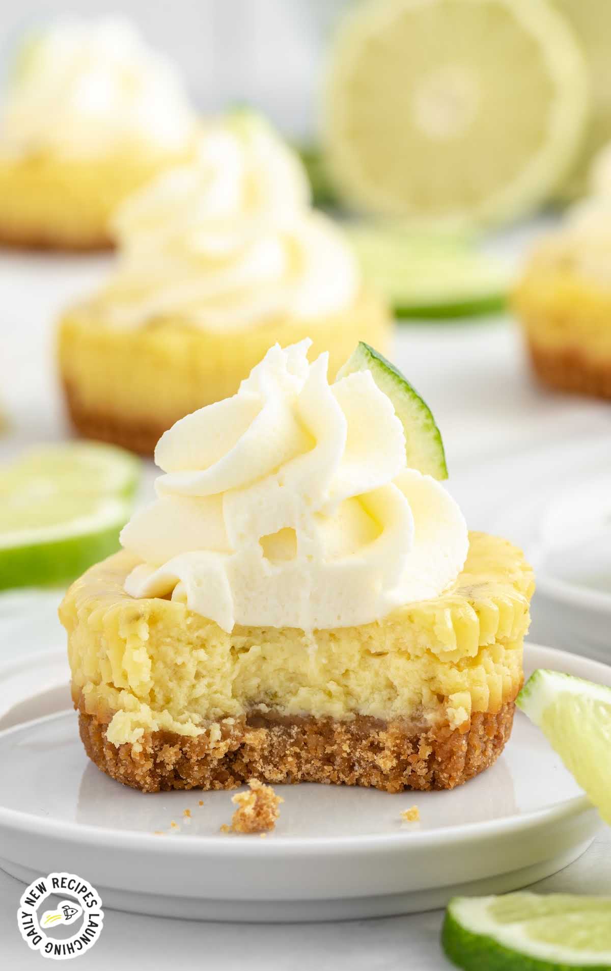 close up shot of Mini Key Lime Pies topped with a slice of lime on a plate and a bite taken out of it