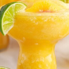 close up shot of Peach Margaritas in a glass topped with a slice of lime and peach