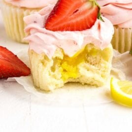 a close up shot of Strawberry Lemon Cupcake topped with a strawberry with a bite taken out of it