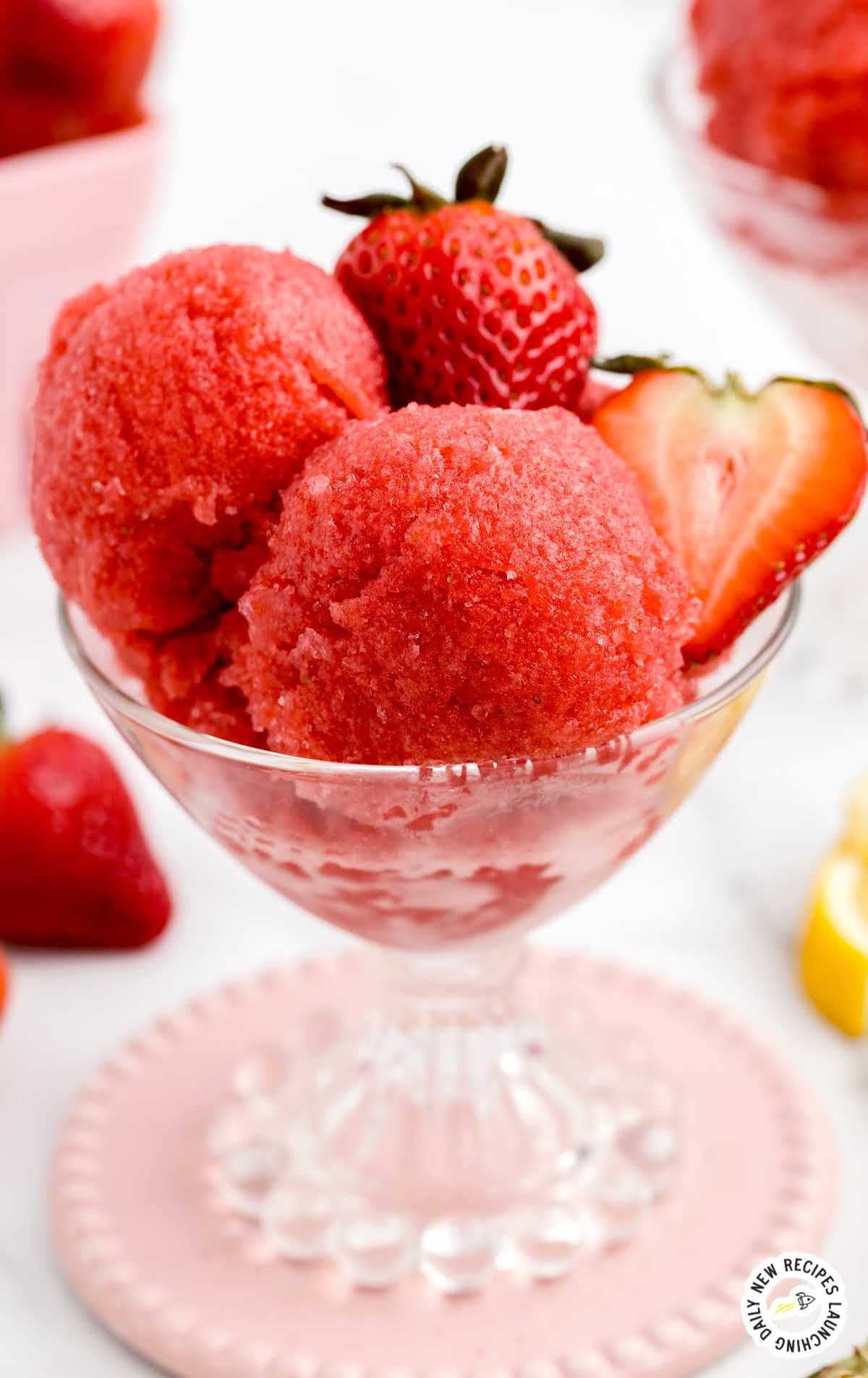 close up shot of scoops of Strawberry Sorbet in a pan along with slices of strawberries in a glass