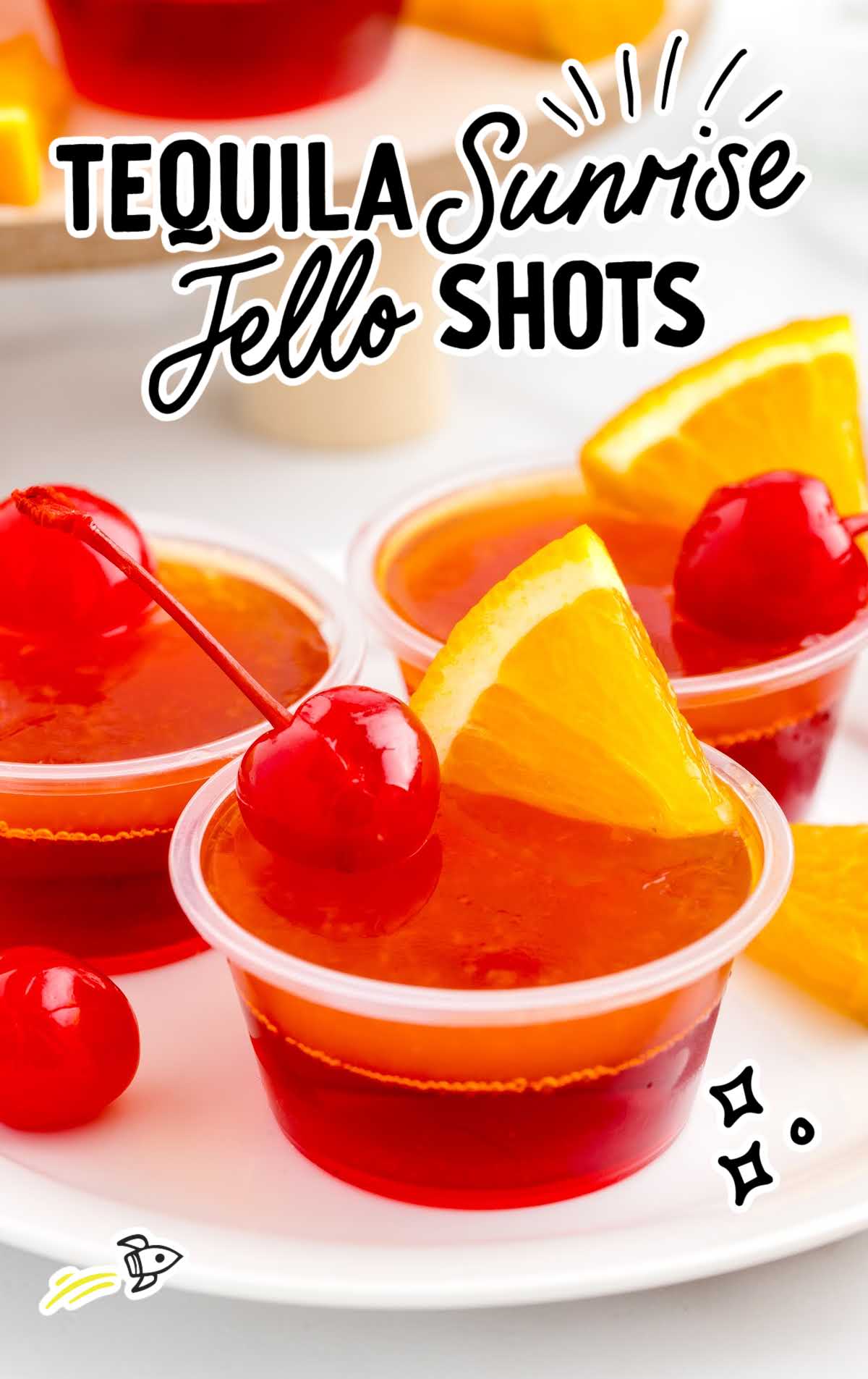 a bunch of containers of Tequila Sunrise Jello Shots topped with cherry and a slice of orange on a plate