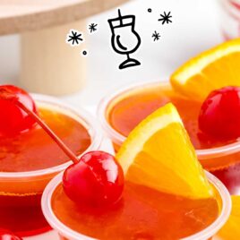 a container full of Tequila Sunrise Jello Shots topped with an orange slice and cherry on a plate