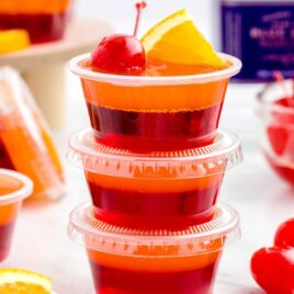 close up shot of containers of Tequila Sunrise Jello Shots stacked on top of each other topped with an orange slice and cherry