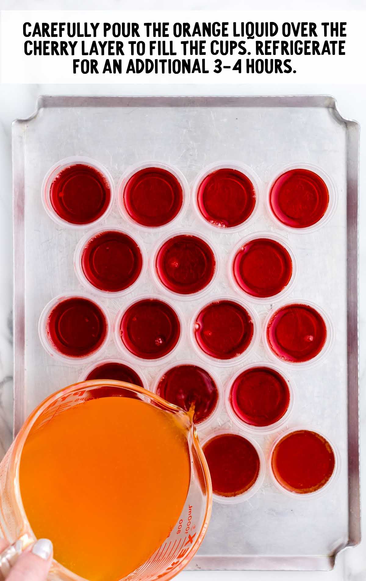 orange liquid poured over the cherry layer to fill cup on a baking sheet