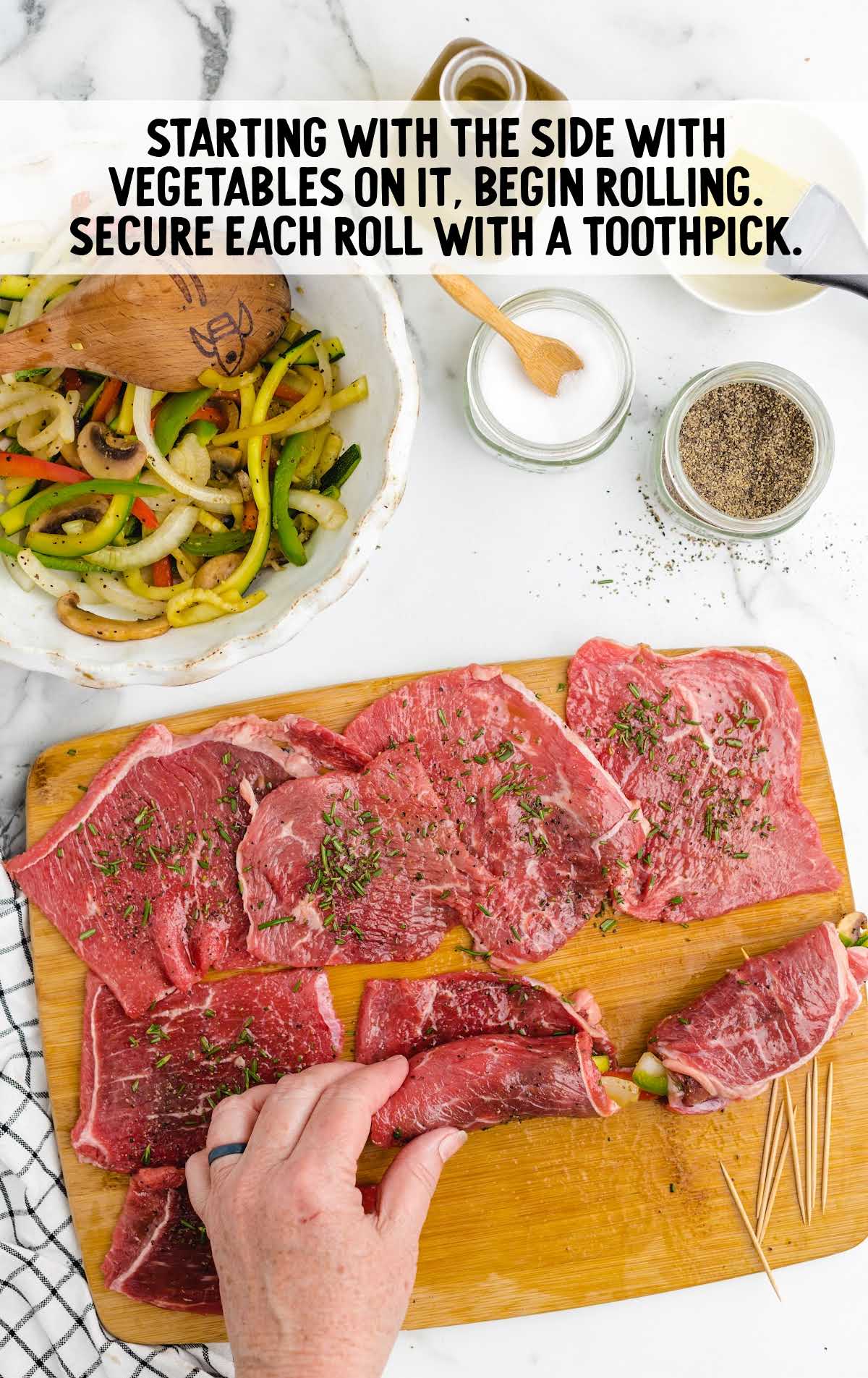 rolling each steak roll with the vegetables on a cutting board