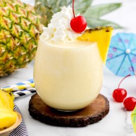 close up shot of Boozy Dole Whip in a glass topped with a slice of pineapple, whipped cream and cherry.