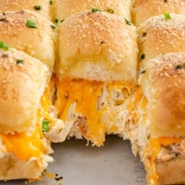Crack Chicken Sliders are cheesy chicken sliders topped with herbs and grated cheese, with one slider pulled out to reveal melted cheddar and creamy chicken filling inside fluffy golden buns.