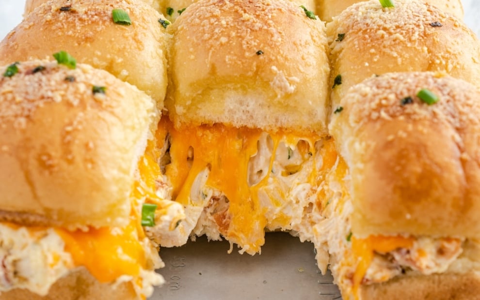 Crack Chicken Sliders are cheesy chicken sliders topped with herbs and grated cheese, with one slider pulled out to reveal melted cheddar and creamy chicken filling inside fluffy golden buns.